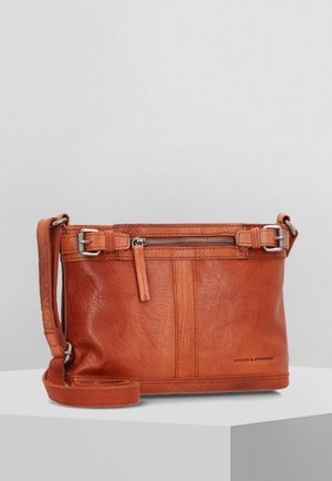Sac bandoulière en cuir marron avec poche avant zippée, sangle réglable et boucles argentées sur une surface blanche.