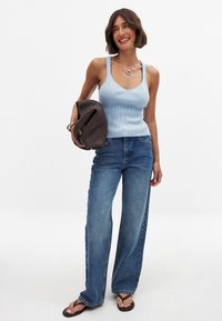 Light blue ribbed tank top, loose-fitting light wash denim jeans, and a woven dark brown handbag, paired with black flip-flops.
