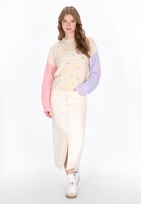 Maglione a maglia con maniche multicolori, corpo beige e motivi a stella ricamati, abbinato a una gonna midi crema e sneakers bianche.