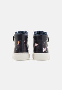Zapatos de niña de color azul marino, tipo botín alto, con suelas blancas, que presentan coloridos patrones de unicornios y estrellas, y un suave forro interior de color azul oscuro, vistos desde atrás.