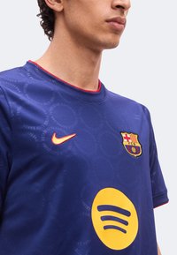 Άνδρας που φοράει μπλε φανέλα ποδοσφαίρου FC Barcelona με κόκκινο λογότυπο Nike και μεγάλο κίτρινο λογότυπο Spotify μπροστά.