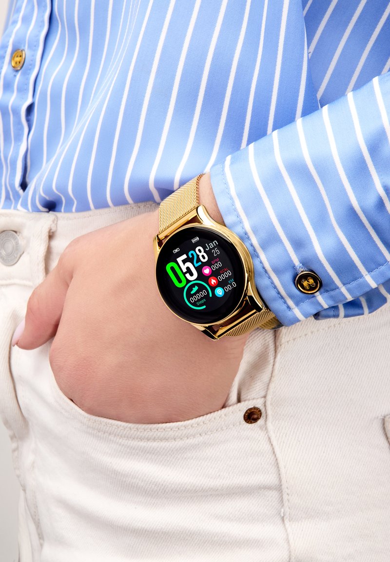 Montre intelligente en or avec un cadran rond et un écran numérique, dotée d'un bracelet en maille. L'écran affiche la date, l'heure et les données de fitness sur un fond noir.