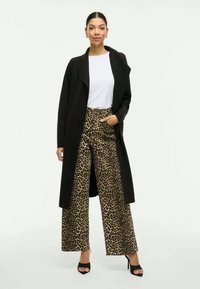 Svart lang kåpe, hvit topp og vide bukser med leopardmønster. Egenskaper inkluderer glatt stoff, kontrastfarger og åpen front på kåpen.