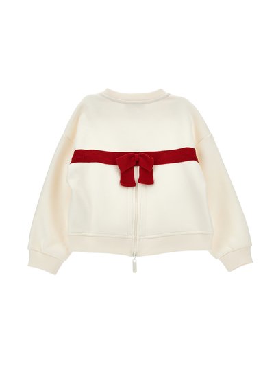 Pull zippé couleur crème à manches longues avec un détail de nœud en velours rouge horizontal sur le haut du dos.