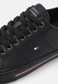 Musta nahkakengät paksuilla mustilla nauhoilla, metallisilla silmukoilla ja brodeeratulla logolla. Ominaisuuksiin kuuluu teksturoitu pohja, jossa on punaisia ja valkoisia korostusraitaja.