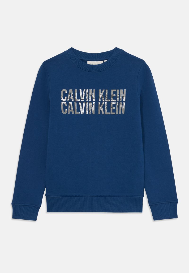 Blågenser laget av bomull, med rund hals, ribbestrikkede mansjetter og kant. Framsiden viser "CALVIN KLEIN" i metallisk trykk.