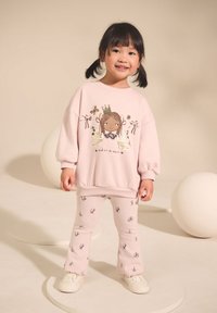 Hellrosa Sweatshirt mit einer Grafik eines Mädchens und Blumenakzenten, kombiniert mit passenden gerippten Leggings mit kleinen Pflanzenmotiven.