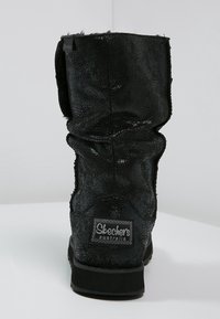 Czarne, sztuczne skórzane botki za kostkę o luźnym fasonie, z fakturowanym wykończeniem i naszywką z logo Skechers z tyłu. Solidna czarna podeszwa.