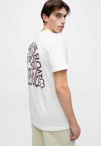 T-shirt branca de algodão com gola redonda e mangas curtas. Apresenta uma grande estampa gráfica bordô nas costas com desenhos abstratos.