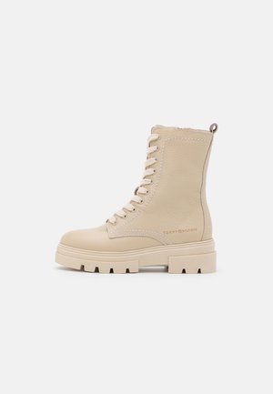 Beżowy skórzany wojskowy but na sznurowadła z masywną podeszwą i suwakiem z boku, z logo Tommy Hilfiger w pobliżu pięty.