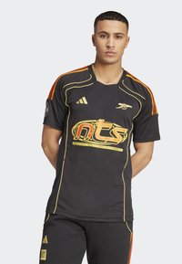 Black athletic jersey featuring yellow accents and a colorful "nts" graphic. Short sleeves, crew neckline, with red and orange stripes on the shoulders.