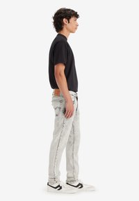 Black short-sleeve t-shirt paired with high-waisted light grey jeans, featuring a slight acid wash and white sneakers with black accents.