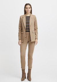 Blazer beige con solapas de muesca, combinado con una camisa de rayas de manga larga y pantalones jogger beige a juego. Botines de punto texturizado hasta el tobillo.