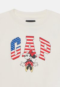 Felpa bianca con le lettere "GAP" in rosso e blu a strisce. Cartone animato di Minnie Mouse con un fiocco rosso e un vestito a pois al centro.