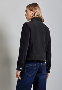 Svart mockajacka med krage och knappade muddar, med en åtsittande design och baktill skärning, tillsammans med mörka jeans.