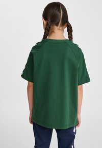 Camiseta de algodón verde con mangas cortas, que presenta un diseño raglán y un ribete en contraste. Textura suave, corte casual y sin logotipos visibles.