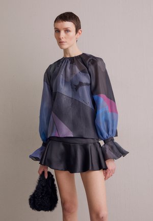 Blouse noire transparente avec des motifs géométriques colorés et des manches bouffantes, associée à une courte jupe en satin noir et un accessoire noir duveteux.