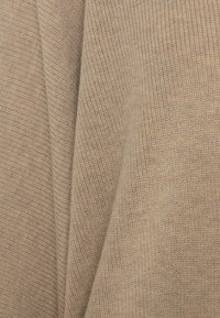 Beige textiel met een diagonale breipatronen en een zachte, warme uitstraling, die subtiele variaties in kleur en draaddiepte toont.