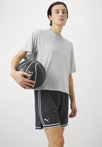 Hallituspruuni lühikeste varrukatega sportlik särk, mis on sobitatud mustade lühikesed püksidega, millel on valged külgribad. Mudel hoiab musta korvpalli.