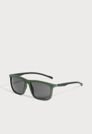 Lunettes de soleil à monture verte, verres gris foncé et embouts de branches noirs, sur fond clair.