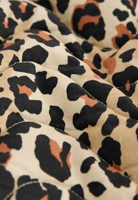 Tela de estampado de leopardo con manchas alternas en negro, beige y color óxido. Textura suave con secciones acolchadas y cosidas.
