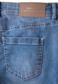 Ljusblå denimjeans med en läderetikett som säger "STREET ONE," med en bakficka och synliga söm detaljer.