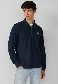Navy Zip-Polohemd mit geripptem Kragen und Bündchen, versehen mit einem kleinen Logo auf der linken Brust und einem strukturierten Stoffdesign.