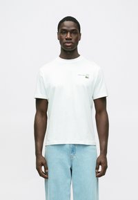 Biała bawełniana koszulka z okrągłym dekoltem, krótkimi rękawami i wytłaczanym logo Lacoste na piersi. W zestawie z jasnoniebieskimi dżinsami.