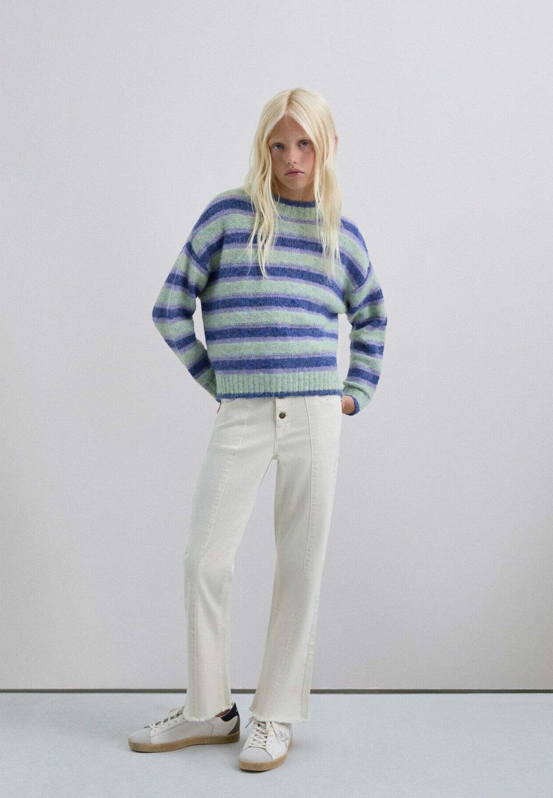 Suéter de punto con rayas horizontales azules y verdes, combinado con jeans acampanados de color blanco roto y zapatillas blancas. Textura suave, ajuste casual.