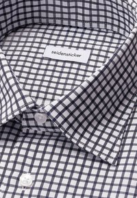 Biała koszula w granatową kratkę, z klasycznym kołnierzykiem i białymi guzikami. Etykieta informuje "seidensticker". Wykonana z tkaniny tkanej.