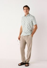 Camisa de manga corta, de color azul claro y con un patrón; tejido de punto con acentos florales. Pantalones sueltos de color beige y sandalias marrones.