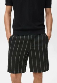 Pantaloni scurți cu dungi alb-negru, confecționați dintr-un material ușor, având două buzunare laterale și o margine curată. Purtați cu un top tricotat negru.