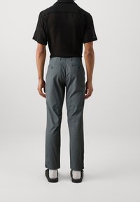Maglietta nera a maniche corte in maglia; pantaloni grigi su misura con una texture liscia e due tasche sul retro; indossati con calzature casual.