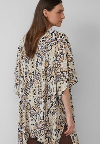 Losse kimono van lichtgewicht stof, met een geometrisch patroon in crème, zwart en oranje. De randen zijn gefranjerd voor textuur.