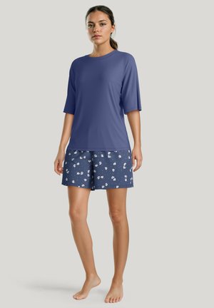 Blauwe top met korte mouwen, gecombineerd met marineblauwe shorts met een wit bloemenpatroon. De stof lijkt zacht; het ontwerp is casual en losvallend.
