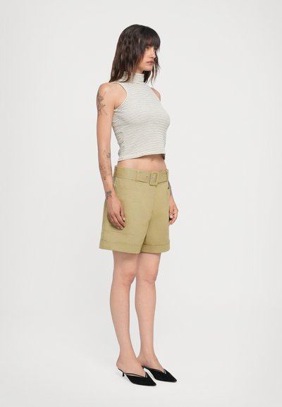 Gestreiftes Cropped-Top in Weiß und Grau, kombiniert mit hoch taillierten olivgrünen Shorts mit einem breiten Gürtel und umgeschlagenen Säumen. Schwarze spitze Absätze.