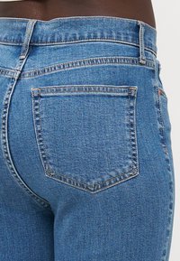 Modré džíny z denimu s priliehavým strihom, stredne vysokým pásom a dvoma zadnými vreckami s jednoduchým prešívaním. Hladká textúra s miernym vyblednutím.