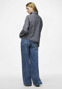 Giubbotto in denim grigio scuro, con colletto classico e maniche lunghe. Abbinato a jeans blu a gamba larga con dettagli di cucitura in vista.