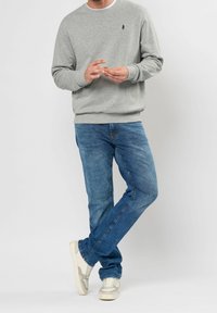 Grijze sweatshirt met geribbelde manchet, gecombineerd met blauwe spijkerbroek en witte sneakers met lichtgrijze accenten. Eenvoudige, casual outfit.