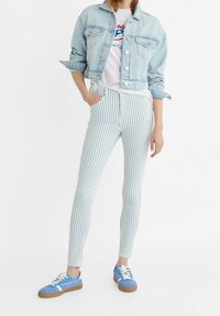 Niebieska dżinsowa kurtka na białym T-shircie, w komplecie z jasnoniebieskimi wąskimi spodniami w pionowe paski i niebieskimi trampkami z beżowymi sznurówkami.