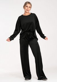 Czarny zestaw lounge składający się z luźnej bluzki z długim rękawem i opadającymi ramionami oraz pasujących spodni z szerokimi nogawkami, wykonany z miękkiego, teksturowanego materiału.