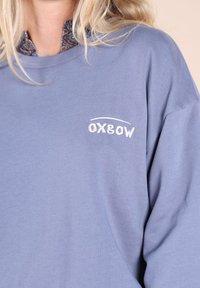 Sweat-shirt bleu clair à manches longues, avec un logo "Oxbow" brodé. Texture douce et col rond standard.
