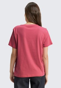 Roze katoenen T-shirt met een losse pasvorm, korte mouwen en een ronde halslijn, van achteren weergegeven tegen een lichtgrijze achtergrond.