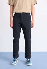 Black, slim-fit trousers with a smooth texture, front button closure, and side pockets, paired with blue and white athletic shoes.