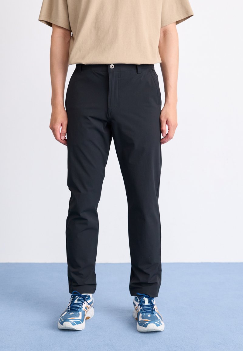 Black, slim-fit trousers with a smooth texture, front button closure, and side pockets, paired with blue and white athletic shoes.