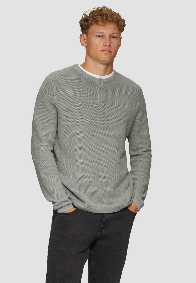 Graues, strukturiertes Langarmshirt mit rundem Halsausschnitt, geknöpfter Lasche und kontrastierendem weißen Kragen. Kombiniert mit schwarzen Hosen.