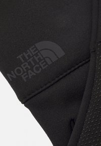 Sort handske med et glat, struktureret stof og et åndbart mesh-panel. Har præget logo fra The North Face.