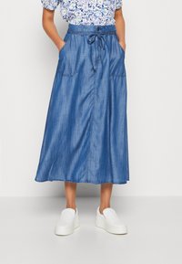 Denim maxikjol med dragsko i midjan, stora sidofickor och en mjuk textur. Färg är medelblå, med en rak silhuett.