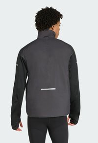 Person facing away wearing a black and dark gray athletic jacket with thumb holes and reflective strips on the back and sleeves.