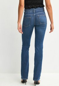 Mörkblå denimjeans med en åtsittande midja och utsvängda ben, med två bakfickor. Tyget har en jämn textur och lätt tänjbarhet.